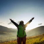 Pessoa de frente para uma paisagem, com os braços abertos