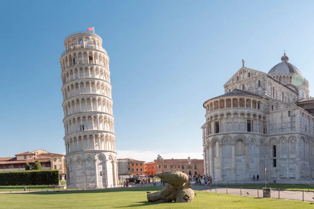Torre de Pisa inclinada ao lado do batistério na Praça dos Milagres com turistas visitando o complexo histórico