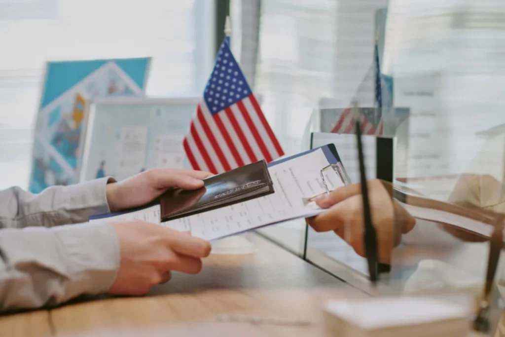 pessoa entregando passaporte e documentos em balcão de atendimento com bandeira dos estados unidos ao fundo