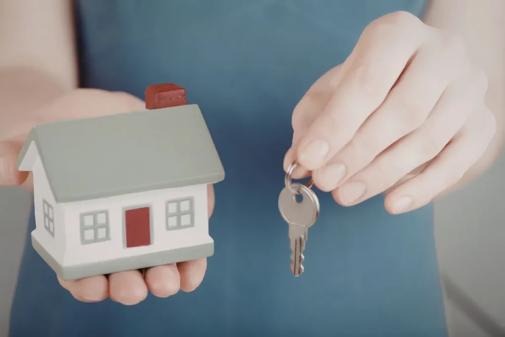 mãos segurando chave e miniatura de casa simbolizando aluguel ou hospedagem