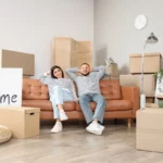 casal sentado em sofá cercado por caixas de mudança em sala organizada