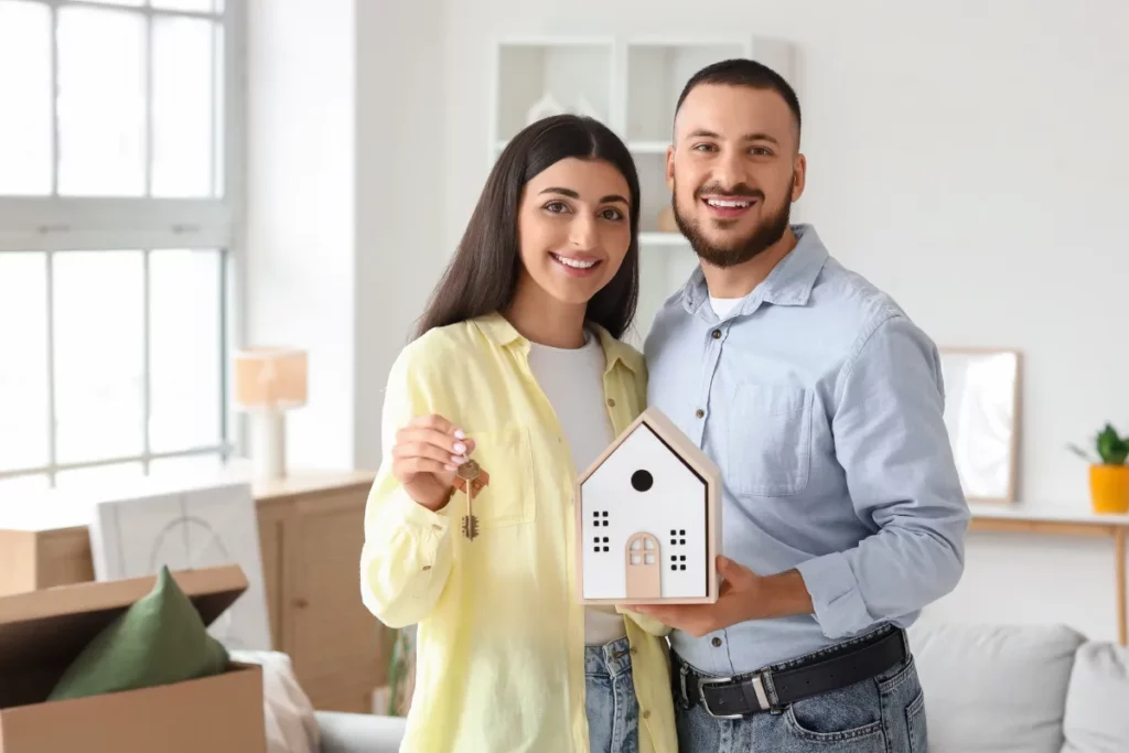 casal sorrindo segurando chave e maquete de casa dentro de ambiente residencial